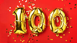 Gold foil balloon number, digit one hundred. Birthday greeting card with inscription 100. Anniversary celebration event. Banner. Golden numeral, red background. Numerical digit, light bokeh, glitter