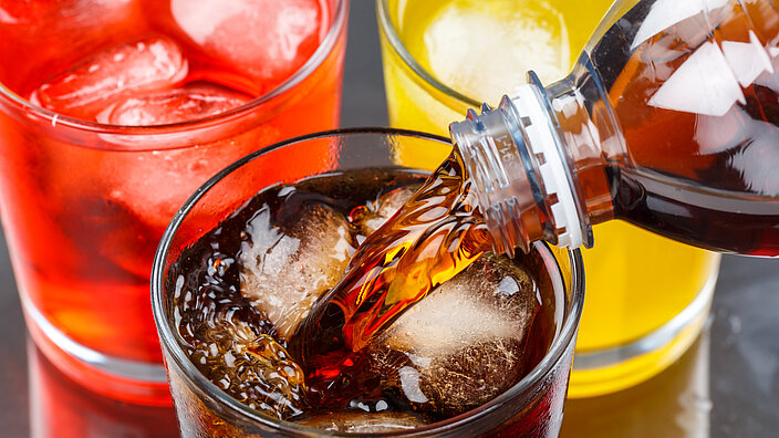 Drei Gläser mit Softdrinks. Aus einer Flasche wird gerade noch Cola in ein Glas geschenkt. 