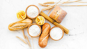 Homemade fresh bread and pasta near flour in bowl and wheat ears on white stone background top view