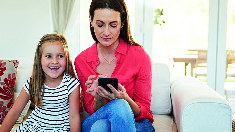Mother, smartphone texting and girl child on sofa happy for love, attention and communication. Woman, online with mobile tech and kid on couch in living room for social media, internet news or email