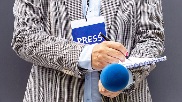 Female journalist at news conference or media event, writing notes, holding microphone