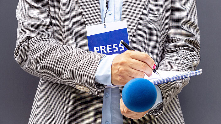 Female journalist at news conference or media event, writing notes, holding microphone